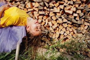 Young funny girl with bright make-up, like fairytale princess, wear on yellow shirt and violet skirt lying against wooden background. photo