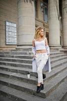 Stylish curly blonde model girl wear on white with cup of coffee posing on stairs outdoor. photo