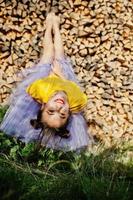 Young funny girl with bright make-up, like fairytale princess, wear on yellow shirt and violet skirt lying against wooden background. photo