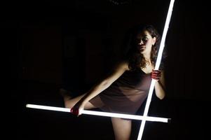 Curly brunette plus size model with two long led lamp at black room. photo