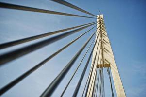 Tall white bridge in a city. Close-up photo of its ropes.