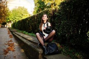 Stylish brunette girl wear on leather jacket and shorts sitting at street of autumn city. photo