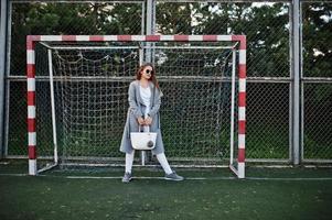 Girl in gray coat with sunglasses at small street stadium football gates. photo