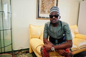 Rich african man sitting on sofa at his appartment. Portrait of successful black man indoor. photo