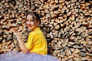 Young funny girl with bright make-up, like fairytale princess, wear on yellow shirt and violet skirt against wooden background. photo