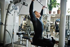 Muscular arab man training and doing workout on fitness machine in modern gym. photo