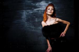 Fashion model red haired girl with originally make up like leopard predator against steel wall. Studio portrait. photo