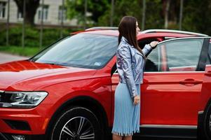 Outdoor photo of gorgeous woman posing near orange suv car with open door.