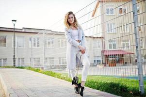 Stylish curly blonde model girl wear on white posing against fence. photo