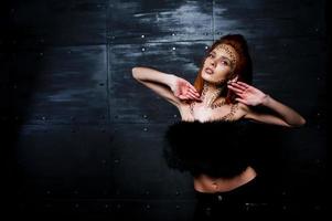 Fashion model red haired girl with originally make up like leopard predator against steel wall. Studio portrait. photo