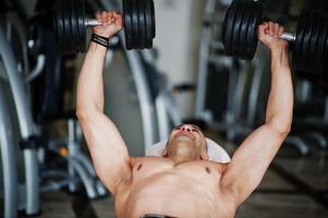 hombre árabe musculoso entrenando con pesas gimnasio moderno. hombres árabes fitness con el torso desnudo haciendo ejercicio. foto