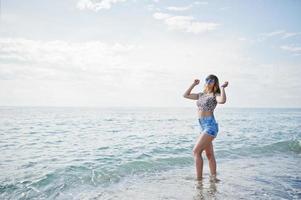 hermosa modelo relajándose en una playa de mar, usando jeans cortos, camisa de leopardo y gafas de sol. foto