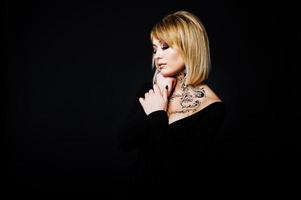 Studio portrait of blonde girl with originally make up on neck, wear on black dress at dark background. photo