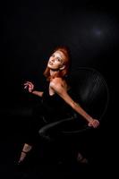 Fashion model red haired girl with originally make up like leopard predator isolated on black. Studio portrait on chair. photo