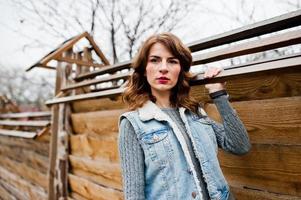 Portrait of brunette curly girl in jeans jacket against wooden wall. photo