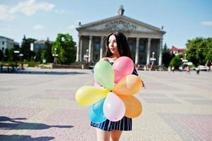 hermosa chica morena en la calle de la ciudad con globos en las manos. foto