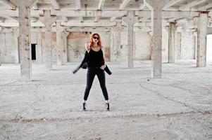 Red haired stylish girl in sunglasses wear in black, against abadoned place. photo