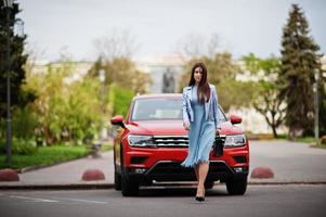 Outdoor photo of gorgeous woman with handbag posing near orange suv car.