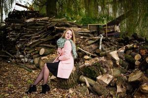 Young blonde girl at pink coat posed against wooden stumps background. photo