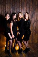 Four cute friends girls wear black dresses against large light christmas star decoration on wooden background. photo