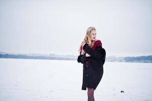 chica rubia de elegancia en abrigo de piel y vestido de noche rojo posó en el día de nieve de invierno. foto