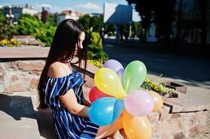 hermosa chica morena en la calle de la ciudad con globos en las manos. foto