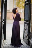 Adult brunette woman at violet gown background black iron gates. photo