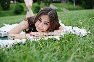 Portrait of a gorgeous woman in black polka dot dress laying next to the books on the blanket on the grass in the park. photo