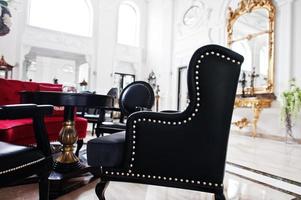 Close-up photo of a black armchair standing in huge white luxurious room.