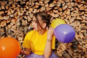 Young funny girl with bright make-up, wear on yellow shirt with colored balloons against wooden background. photo