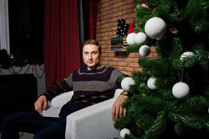 retrato de estudio del hombre contra el árbol de navidad con adornos. foto