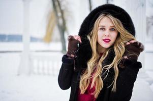 Elegance blonde girl in fur coat and red evening dress posed at winter snowy day. photo