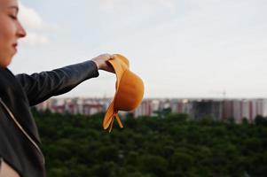 Portrait of an attractive woman waving her orange hat on top of the building in city. photo