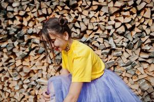 Young funny girl with bright make-up, like fairytale princess, wear on yellow shirt and violet skirt against wooden background. photo