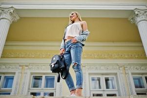 Blonde girl wear on jeans with backpack posed against vintage house. photo