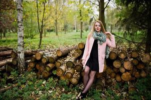 Young blonde girl at pink coat posed against wooden stumps background. photo