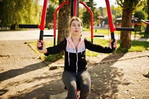 Young girl has the training and doing exercise outdoors on street simulators. Sport, fitness, street workout concept. photo