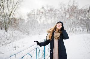 Beautiful brunette girl in winter warm clothing. Model on winter jacket and black hat. photo