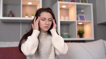 Headache in teenagers. The woman who has a headache at home is holding her head in pain and trying to relax. video