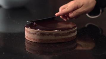 heiße schokolade auf den kuchen gießen. Kuchen machen. Konditormeister. die Szene, in der die Schokolade mit dem Kochmesser darauf getrieben wird. video