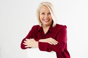 retrato de una alegre y sonriente mujer rubia de mediana edad sentada en una silla aislada en blanco foto