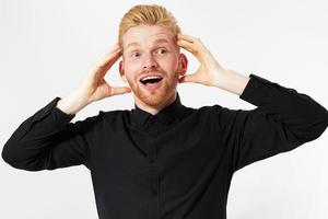 Handsome excited surprised red hair man happy smile looking at camera, hold hands on head, young guy wear black stylish shirt, white teeth, isolated over white background photo