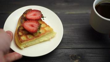Belgian waffles with strawberries and coffee on a wooden, dark table.
