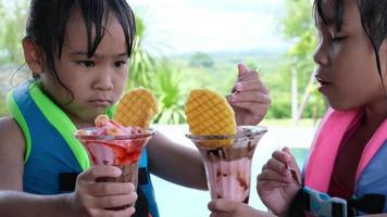 las hermanitas tristes luchan por el helado de chocolate junto a la piscina. hermanas asiáticas peleando por el helado. Relaciones difíciles entre hermanos en la familia. video