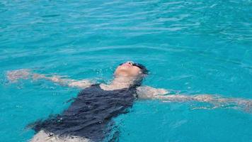 bela jovem asiática feliz e sorria na piscina. mulher asiática em traje de banho está nadando na água limpa azul da piscina para exercício. conceito de viagens e férias de verão. video