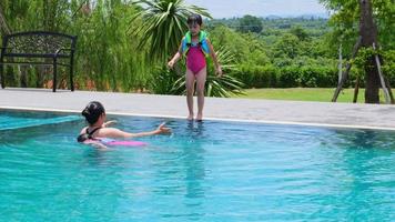 jovem mãe cuida de uma filha que está prestes a pular na piscina. irmãzinhas fofas estão nadando com a mãe na piscina em um dia ensolarado. conceito de estilo de vida de verão. video