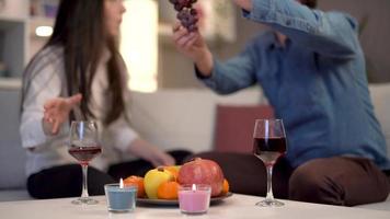 pareja bebiendo vino y comiendo fruta. el feliz estado de la pareja bebiendo vino y consumiendo fruta en casa por la noche. video