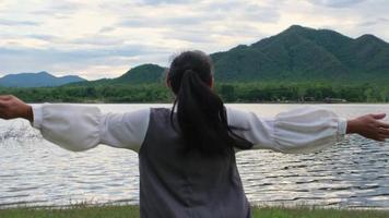 asiatisk kvinna njuter av naturvyn vid sjön vid solnedgången. livsstil och semester resor koncept video