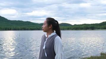 asiatische Frau, die bei Sonnenuntergang die Aussicht auf die Natur am See genießt. Lifestyle- und Urlaubsreisekonzept video