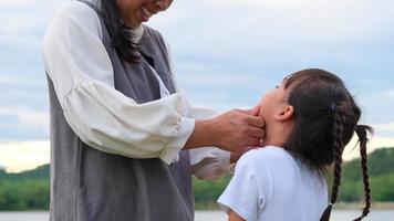 mãe amorosa segurando uma linda garotinha sorridente e beijando à beira do lago. família feliz, mãe e filha brincando se sentindo felizes no parque. video